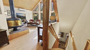 A spacious living area with a large fireplace, wooden flooring, and a staircase leading to an upper level. - Chalet Forest Views, 2 kings, fireplace, decks (Pine)