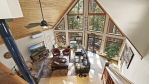 A spacious loft with large windows, a wooden ceiling, and a cozy seating area with a fireplace. - Chalet Forest Views, 2 kings, fireplace, decks (Pine)