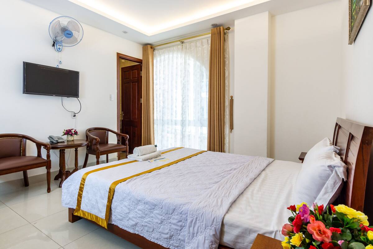 A hotel room with a bed, a desk with a chair, a television, and a window with curtains.