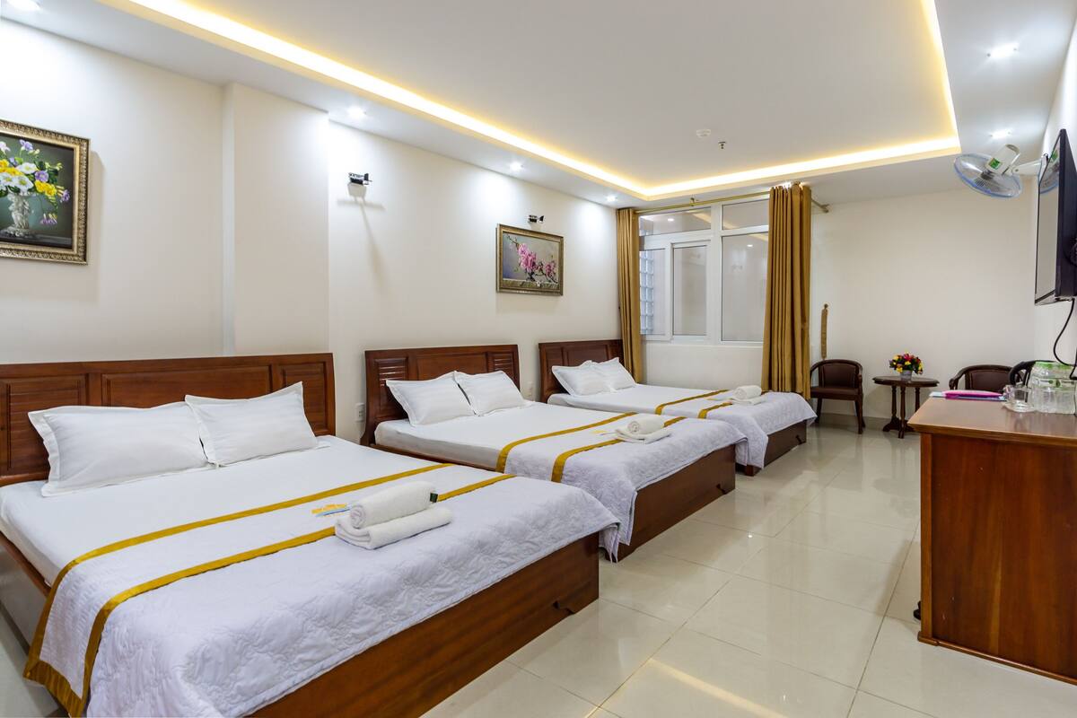 A hotel room with four single beds, a wooden desk, a small table, and a TV mounted on the wall.