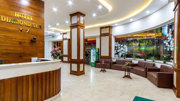 Zona de recepción de un hotel con un mostrador de madera, un área de estar con sofás y un ventanal con detalles florales.