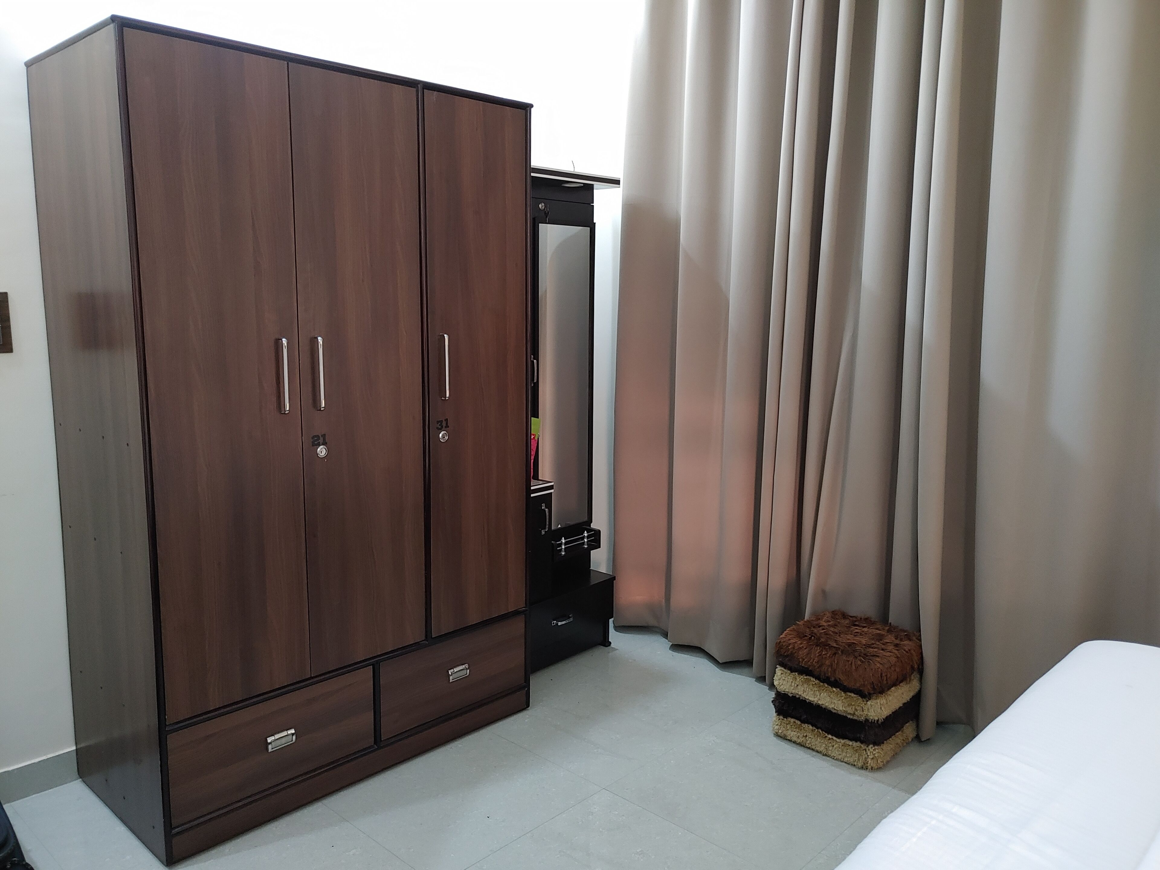 Een slaapkamer met een grote kast, een bed, een klein krukje en een spiegel.