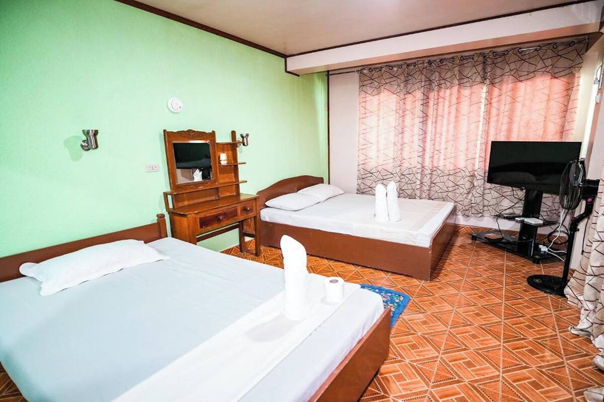 A hotel room with two beds, a TV, a mirror, and a window with curtains.