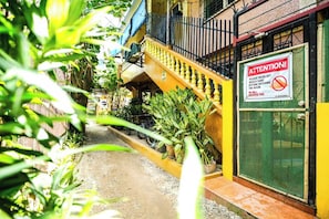 A narrow alleyway with a yellow building, a sign instructing to wash off beach sand before entering, and potted plants along the path. - Gracia's Inn Boracay (Boracay Island)