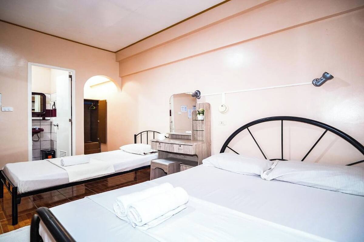 A hotel room with two beds, a small desk, a mirror, and a wall-mounted heater.
