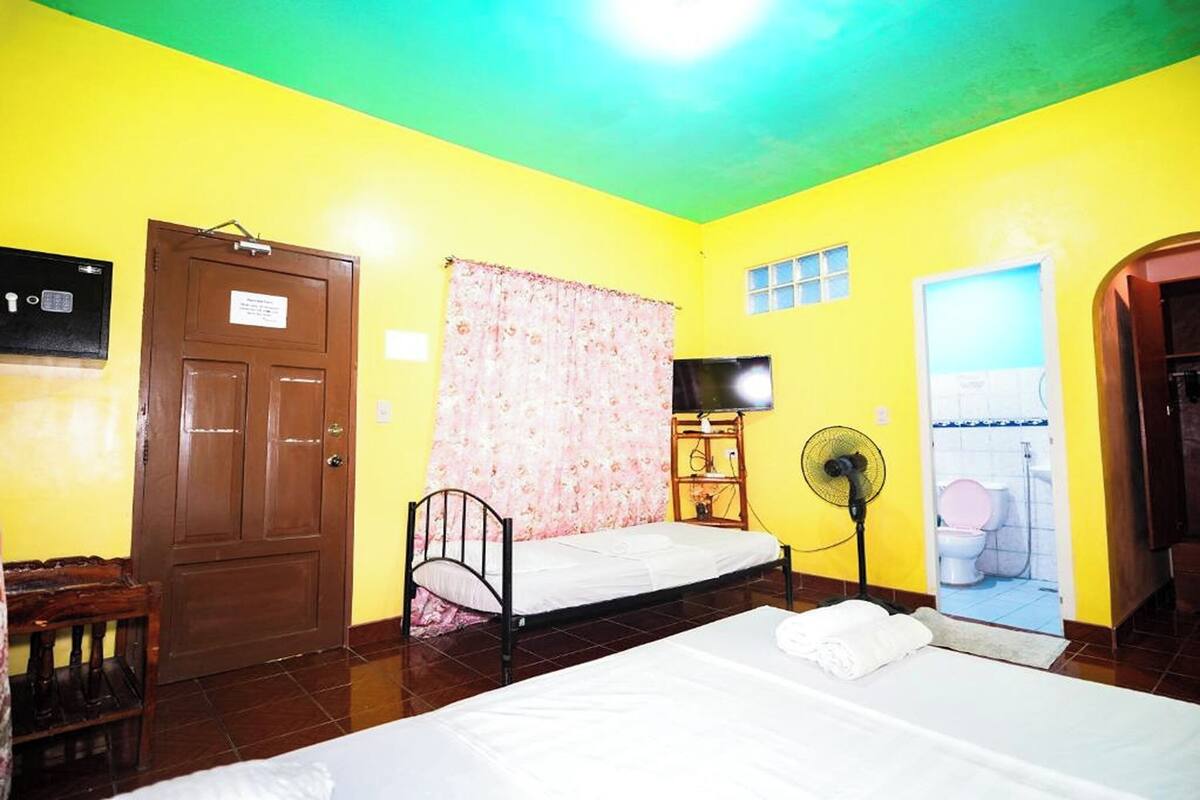 A room with a bed, a wooden door, a fan, and a bathroom visible through an open door.