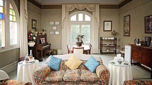 A spacious room with a floral-patterned sofa, a piano, a dining table, and a cabinet. - Forgandenny Bed & Breakfast (Mudgee)