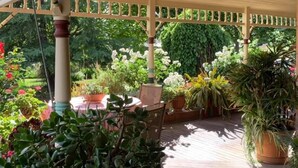 A covered patio area with a wooden deck, a table with chairs, and various potted plants. - Forgandenny Bed & Breakfast (Mudgee)