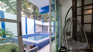 A room with a hanging chair, a view of a swimming pool, and a large window. - 3BU Hostel La Union (San Fernando)
