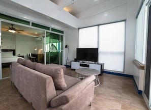 A modern living room with a sofa, a TV, and a glass door leading to another room. - 3BU Hostel La Union (San Fernando)