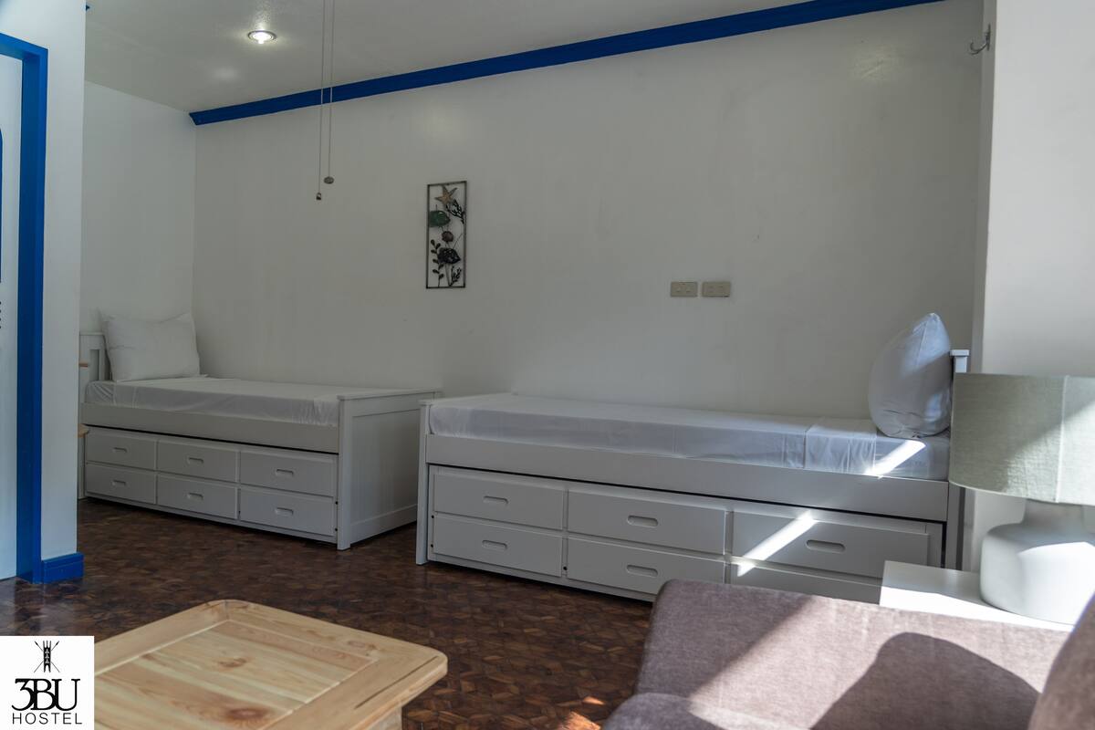 A room with two single beds, a wooden table, and a sofa.