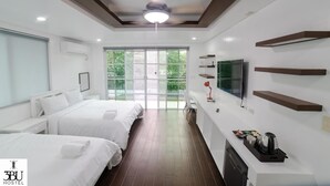 A hotel room with two beds, a TV, a desk, and a window with a view of greenery. - 3BU Hostel La Union (San Fernando)