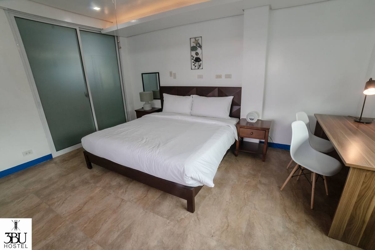 A bedroom with a bed, bedside table, lamp, chair, and a desk.
