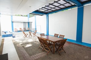 A covered outdoor area with a wooden table and chairs, a pool, and a blue and white color scheme. - 3BU Hostel La Union (San Fernando)