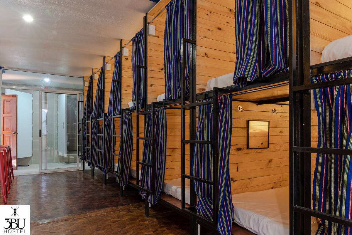 A hostel room with bunk beds, wooden walls, and striped curtains.