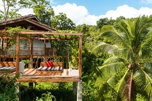 A wooden deck with a bed and a small table, surrounded by lush greenery and a palm tree. - Beso Hilltop Retreat - Hostel (San Vicente)