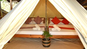 Una carpa con dos camas, cada una con almohadas y una manta. Hay una planta pequeña en una cesta sobre el suelo.