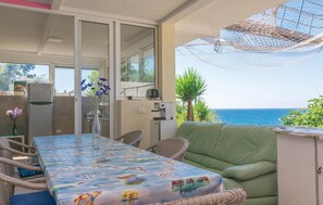 Un patio iluminado por el sol con una mesa cubierta con un mantel colorido, sillas de mimbre, un sofá verde y vistas al mar.