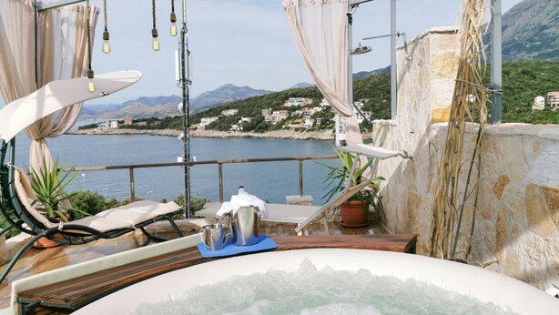 Una terraza en la azotea con jacuzzi, sillas de descanso y vistas al mar y a las montañas.