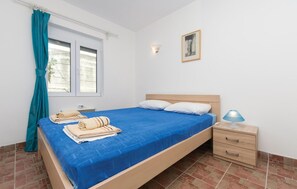 Un dormitorio con cama, mesita de noche, lámpara, ventana con cortinas e iluminación en la pared.