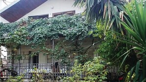 Un edificio con un porche cubierto, una cerca metálica y varias plantas.
