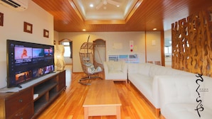 Un salon équipé d’un téléviseur, d’un canapé blanc, d’un plancher en bois, d’un ventilateur de plafond et d’un panneau décoratif mural.
