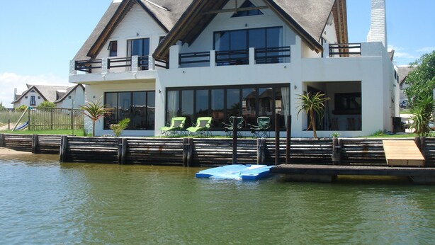 A modern two-story house with a large balcony, large windows, and a dock extending into a body of water. - St Francis Bay House On The Canal (Saint Francis Bay)
