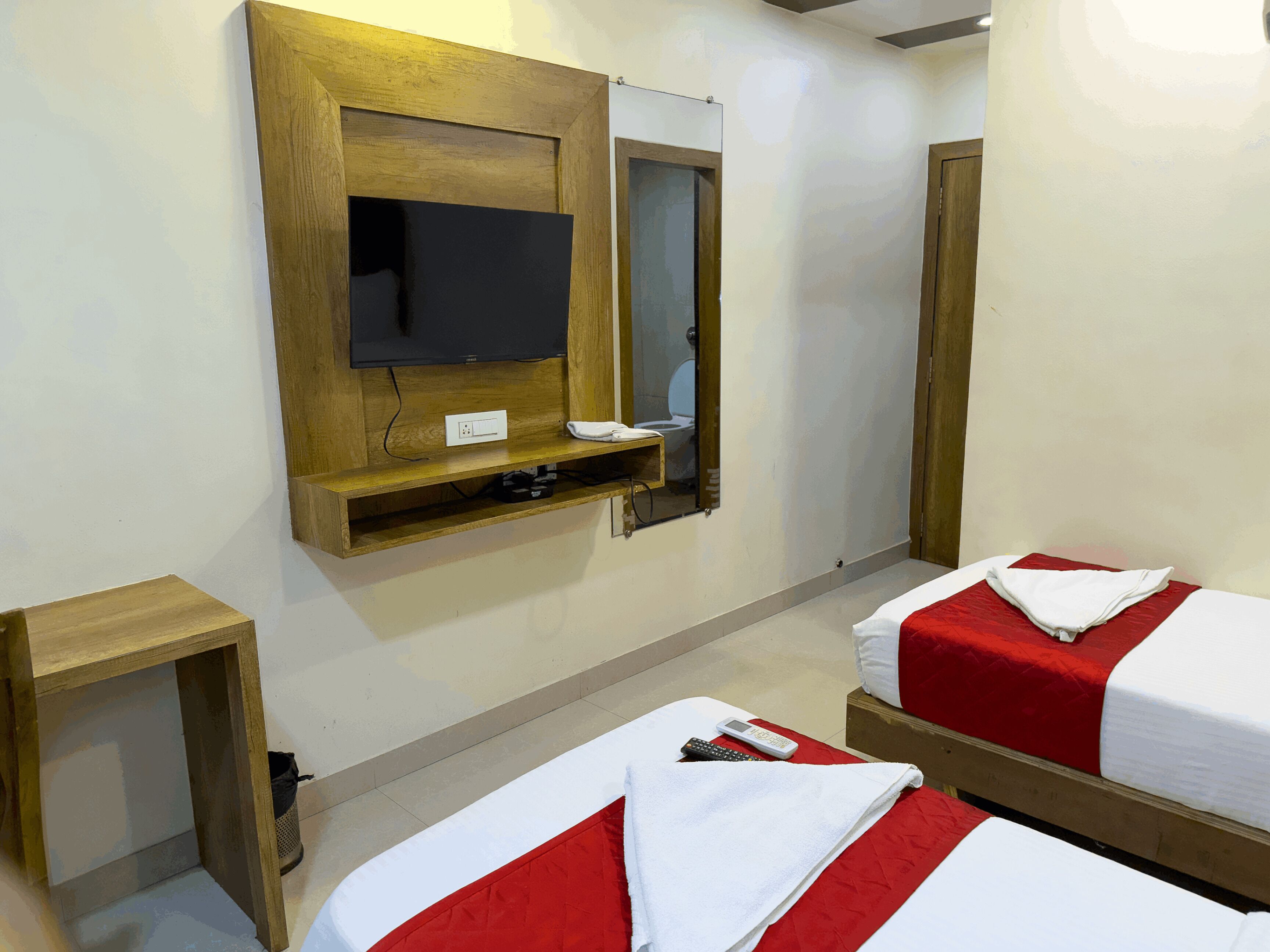 A hotel room with two beds, a TV mounted on the wall, a small wooden table, and a mirror.