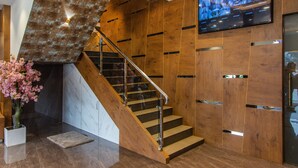 A wooden staircase with glass railings, a marble wall, and a potted plant.