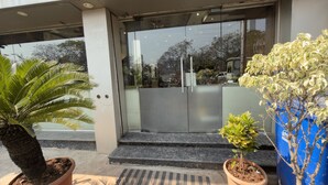 A building entrance with a glass door, steps leading up to it, and potted plants on either side.
