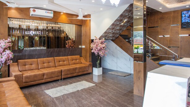 A modern lobby with a brown leather sofa, a white vase with pink flowers, and a wooden staircase.