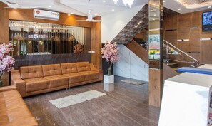 A modern lobby with a brown leather sofa, a white vase with pink flowers, and a wooden staircase.