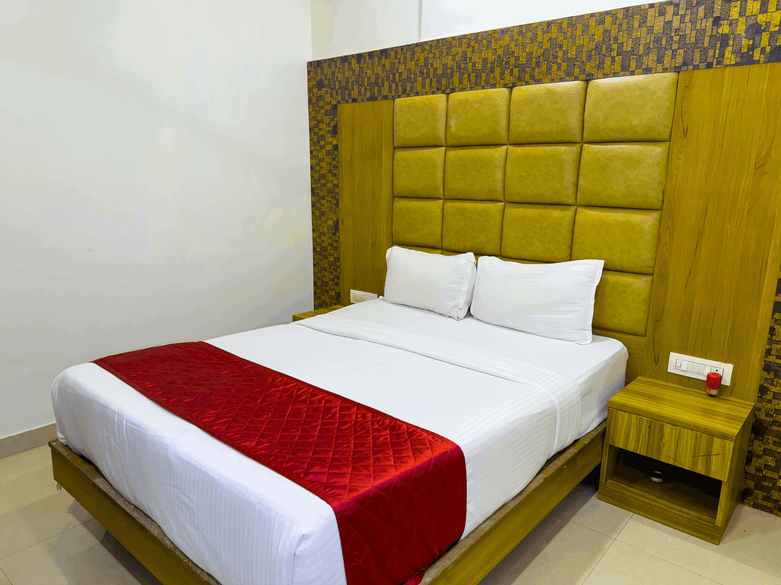 A hotel room with a large bed, a wooden headboard, and a nightstand with a red candle.