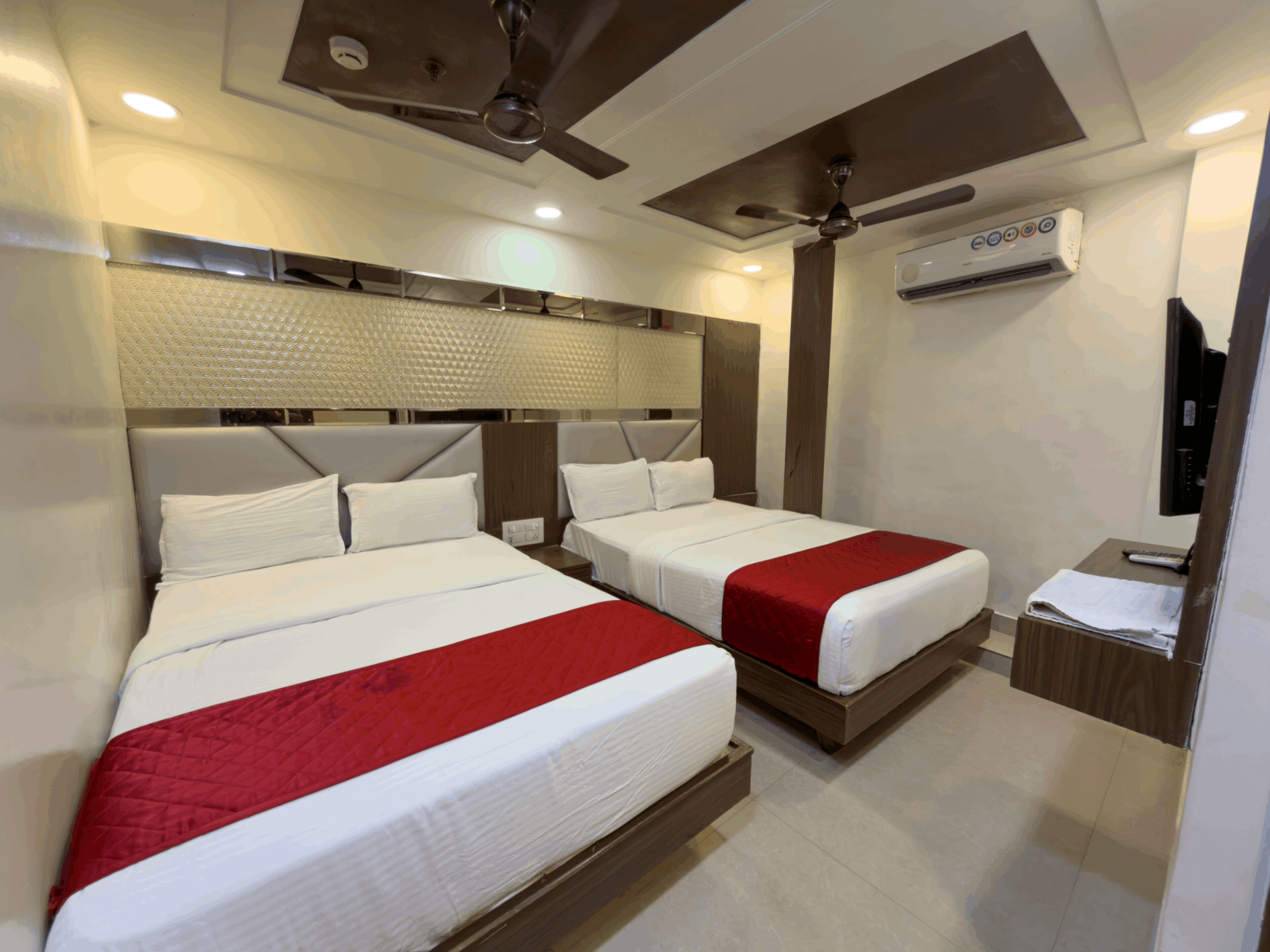 Habitación de hotel con dos camas, un ventilador de techo, un equipo de aire acondicionado y una mesita con un control remoto.