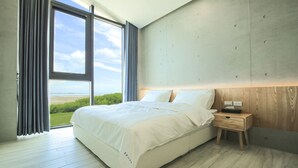 A modern bedroom with a large bed, a wooden nightstand, and a view of the outdoors.