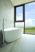 Un baño moderno con una bañera independiente, un ventanal grande y vistas a un paisaje costero.