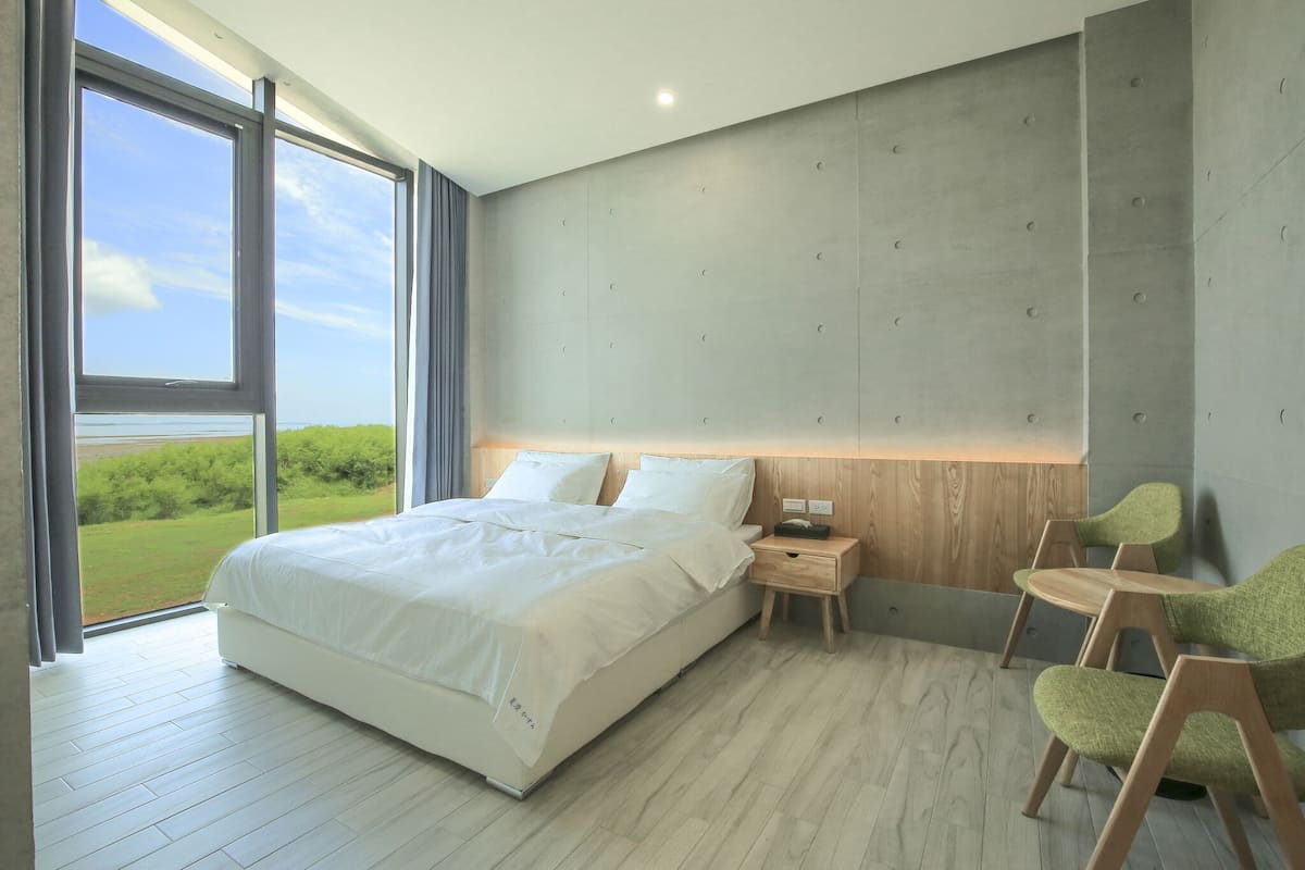 Een moderne slaapkamer met een groot bed, houten nachtkastjes en uitzicht op groen.