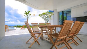 A modern kitchen with white cabinets and a large window overlooking a pool and ocean.