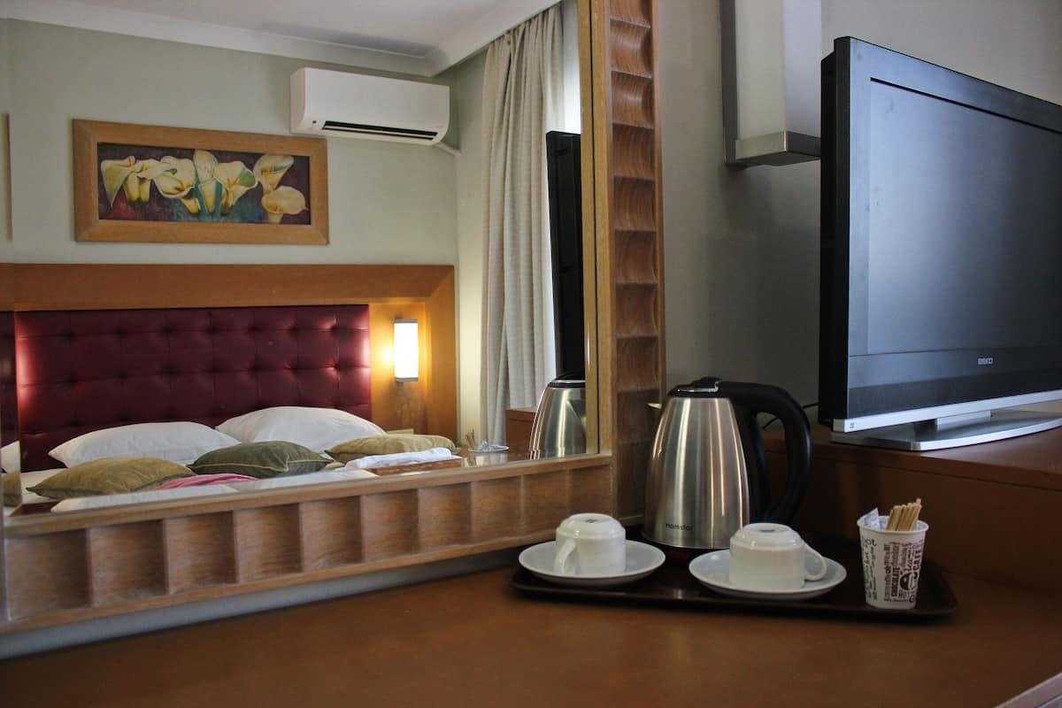 Une chambre d’hôtel avec un lit, une télévision, un plateau de courtoisie avec des tasses et une cafetière, et un tableau accroché au mur.
