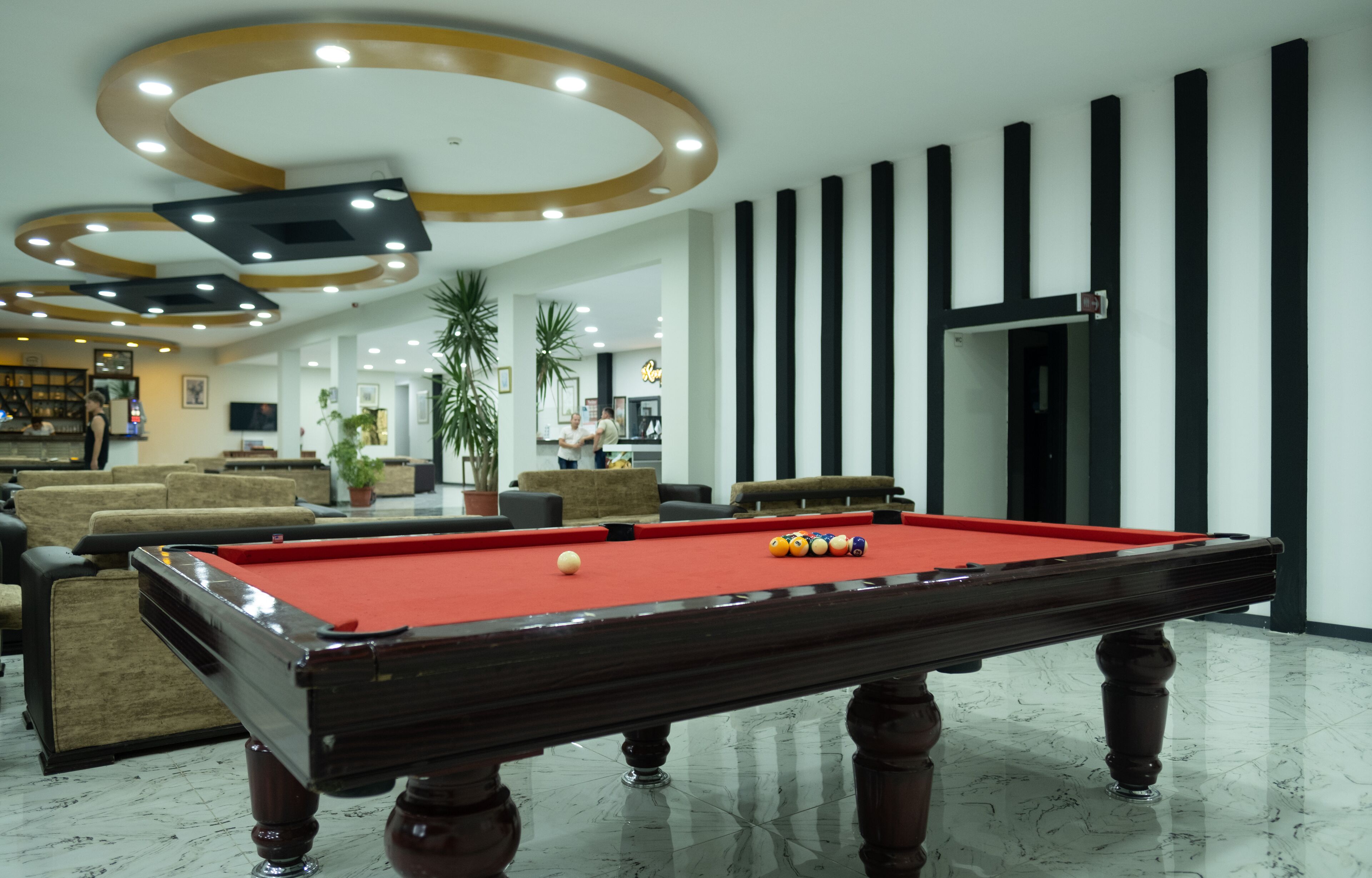 Una mesa de billar en el vestíbulo de un hotel, con un diseño de techo moderno y una zona de estar con sofás.