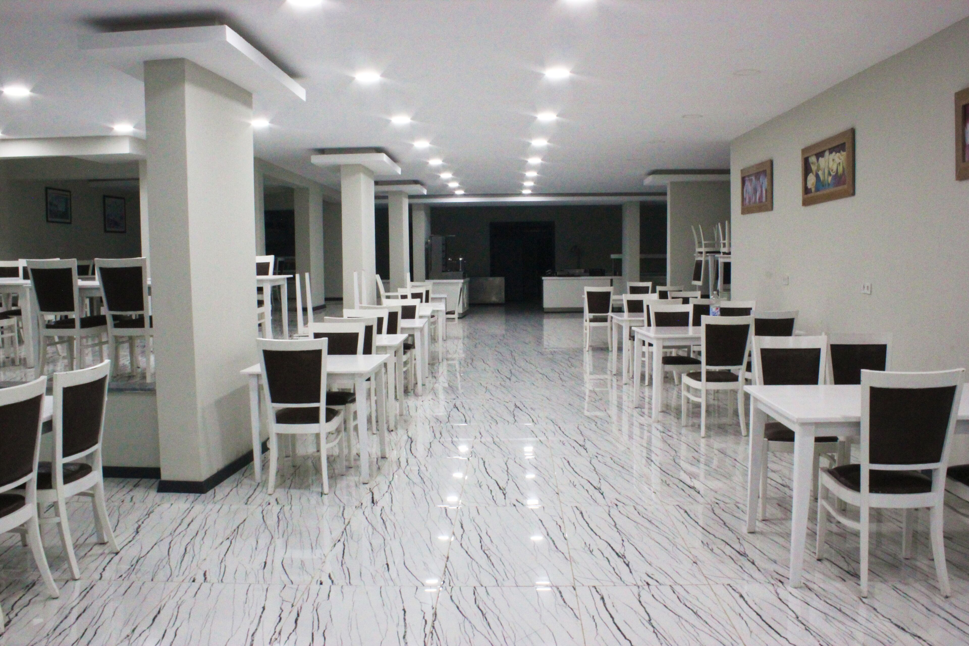 A spacious hall with white tables and chairs arranged in rows, a polished marble floor, and recessed ceiling lighting.