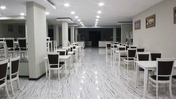 A spacious hall with white tables and chairs arranged in rows, a polished marble floor, and recessed ceiling lighting.
