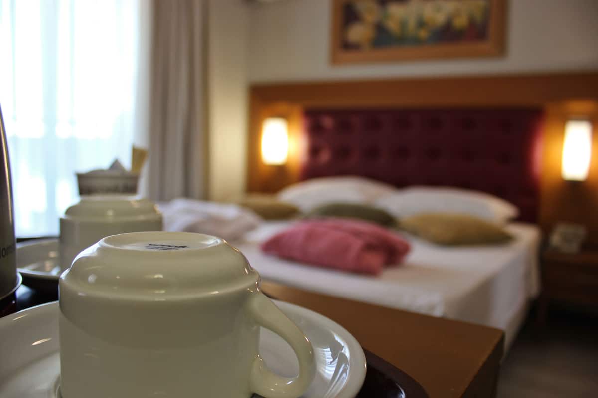 Une chambre d’hôtel avec un lit, des oreillers, une table de chevet et une tasse sur un plateau.