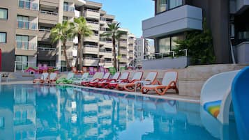 A swimming pool with lounge chairs and palm trees, surrounded by multi-story buildings.