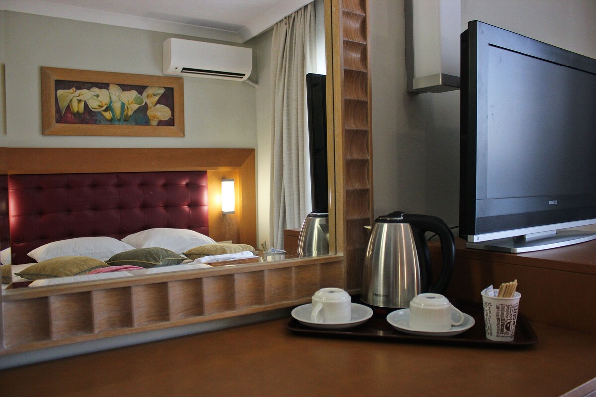 A hotel room with a bed, a television, a coffee tray with cups and a coffee pot, and a painting on the wall.
