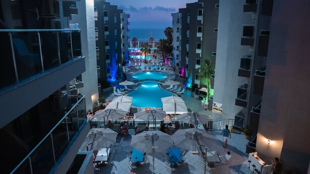 A rooftop pool area with lounge chairs and umbrellas, surrounded by modern buildings.
