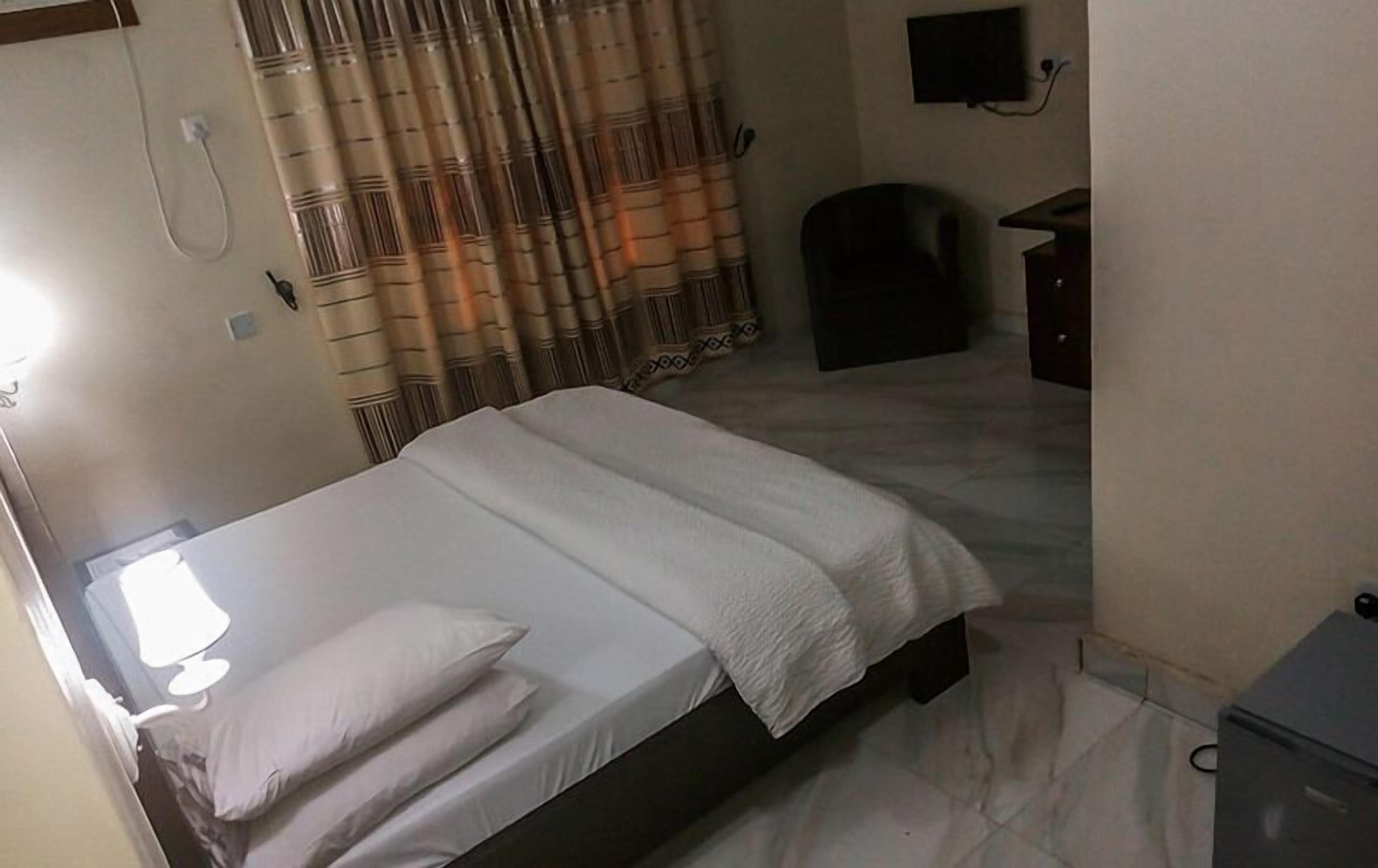 Una habitación de hotel con cama, escritorio, silla, televisor y cortinas.