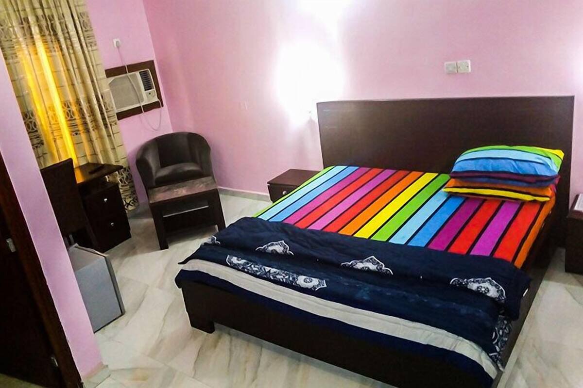 A bedroom with a bed, a chair, a nightstand, and a wall-mounted air conditioner.