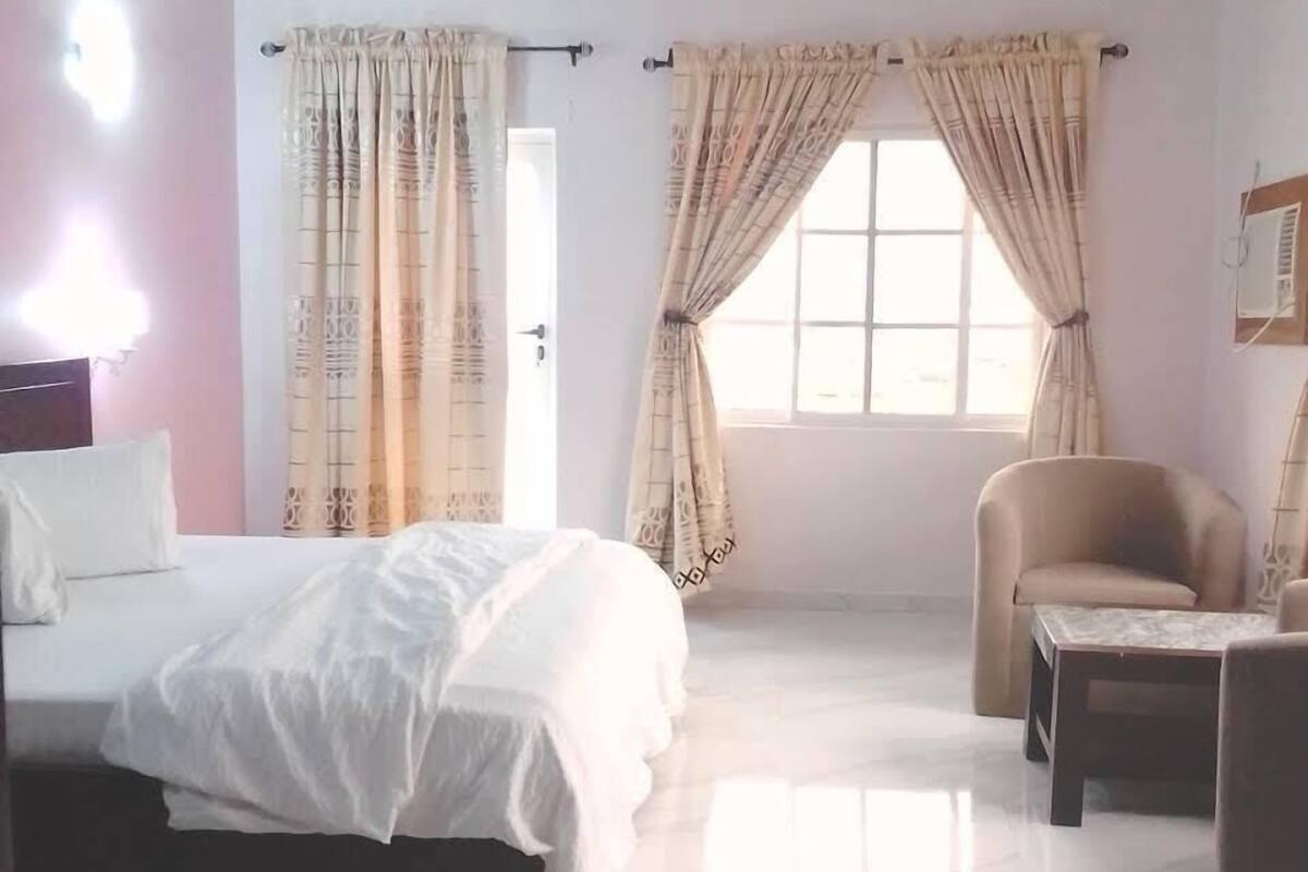A bedroom with a bed, a chair, a small table, and a window with curtains.