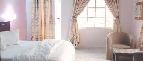 A bedroom with a bed, a chair, a small table, and a window with curtains.